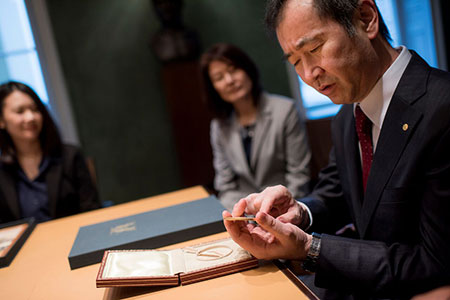 manbet手机版2015年12月12日，Takaaki Kajita在访问诺贝尔基金会期间仔细查看了他的诺贝尔奖章和文凭。